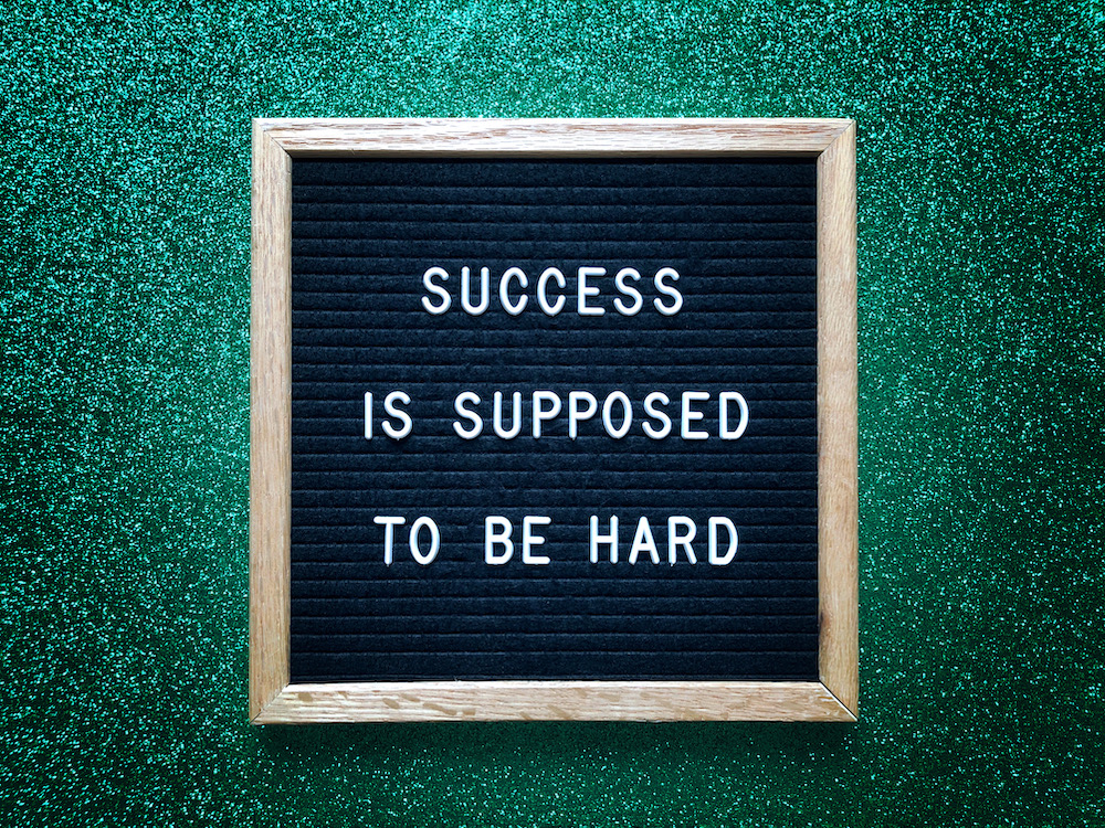 Sign with the phrase "Success is Supposed to Be Hard" on a green background.